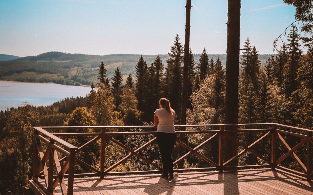 bildet viser en kvinne som står på platting med utsikt over innsjøen Røgden og Finnskogen. hun ser utover.