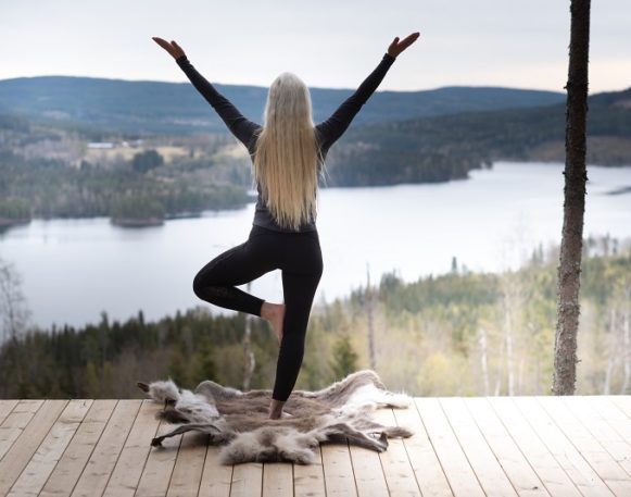 bildet viser en kvinne står i en yogapositur med ryggen til kamera og ser utover Røgden, et vann på Finnskogen.