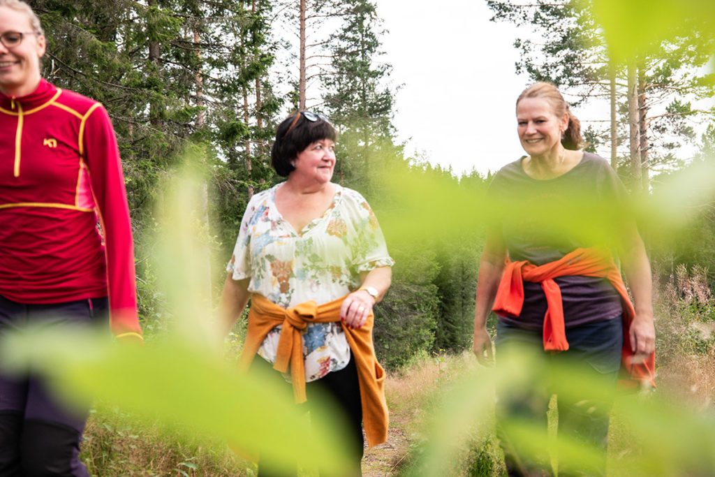 tre kvinner går tur i skogen, blader foran kamera i uskarpt fokus