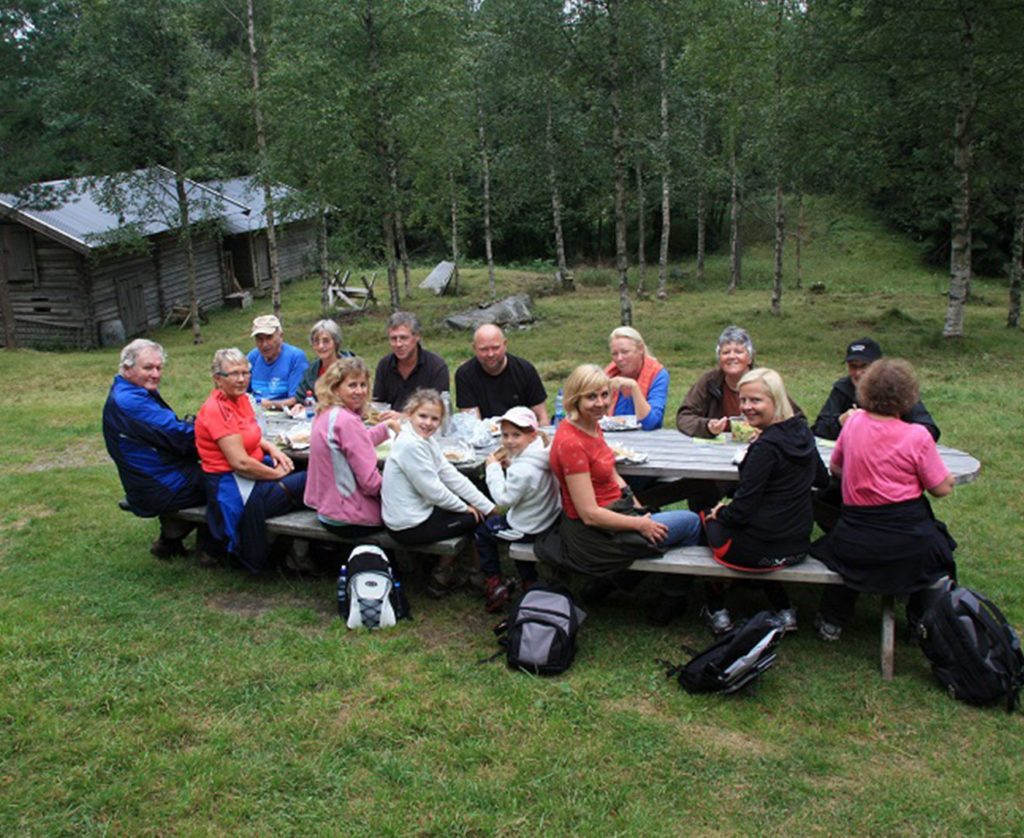 en gjeng spiser lunsj ved et benkebord i skogen